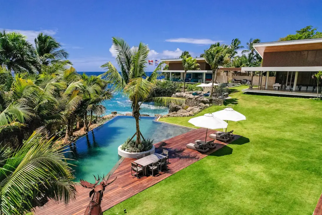 A landscaped outdoor pool beside a wooden deck, lawn, and palm trees.