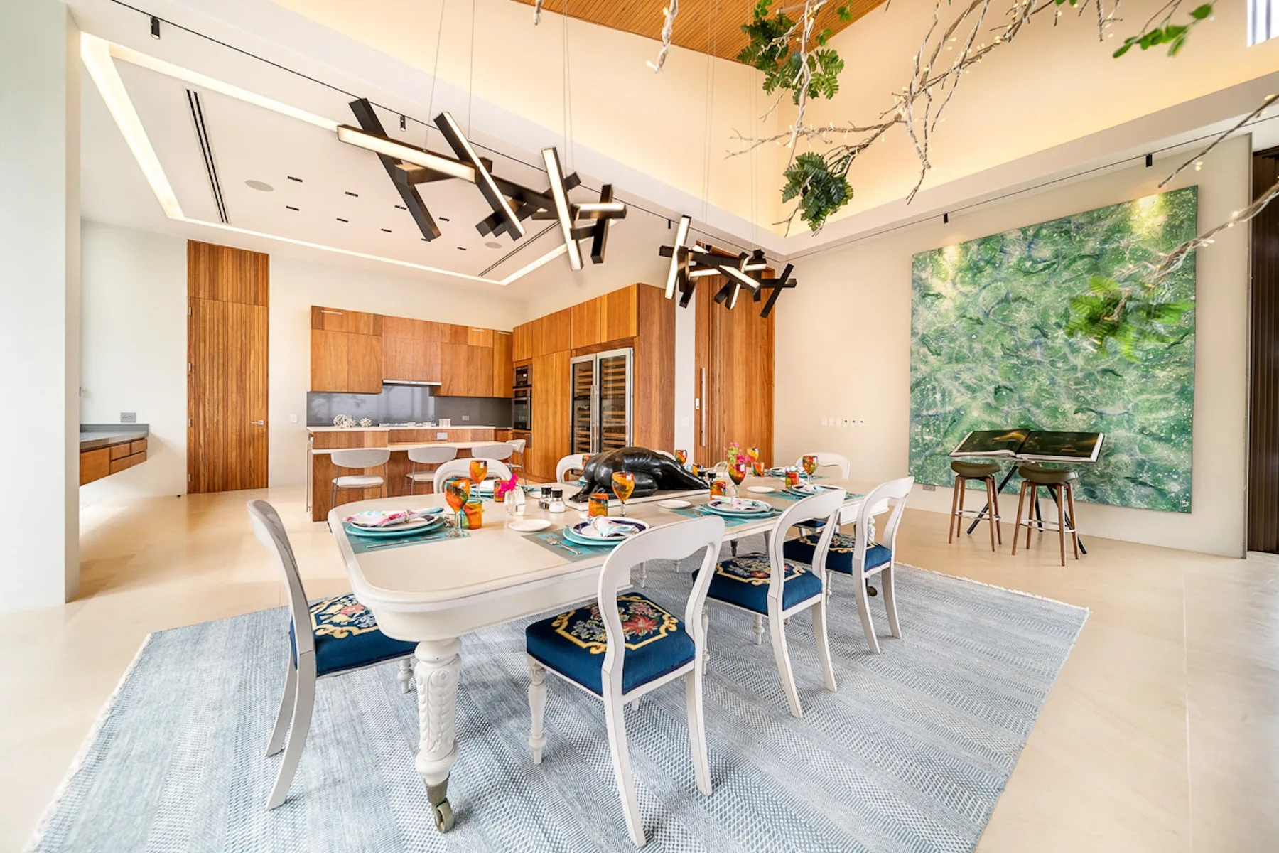 A dining area with a long table, surrounded by seating and set near a kitchen.