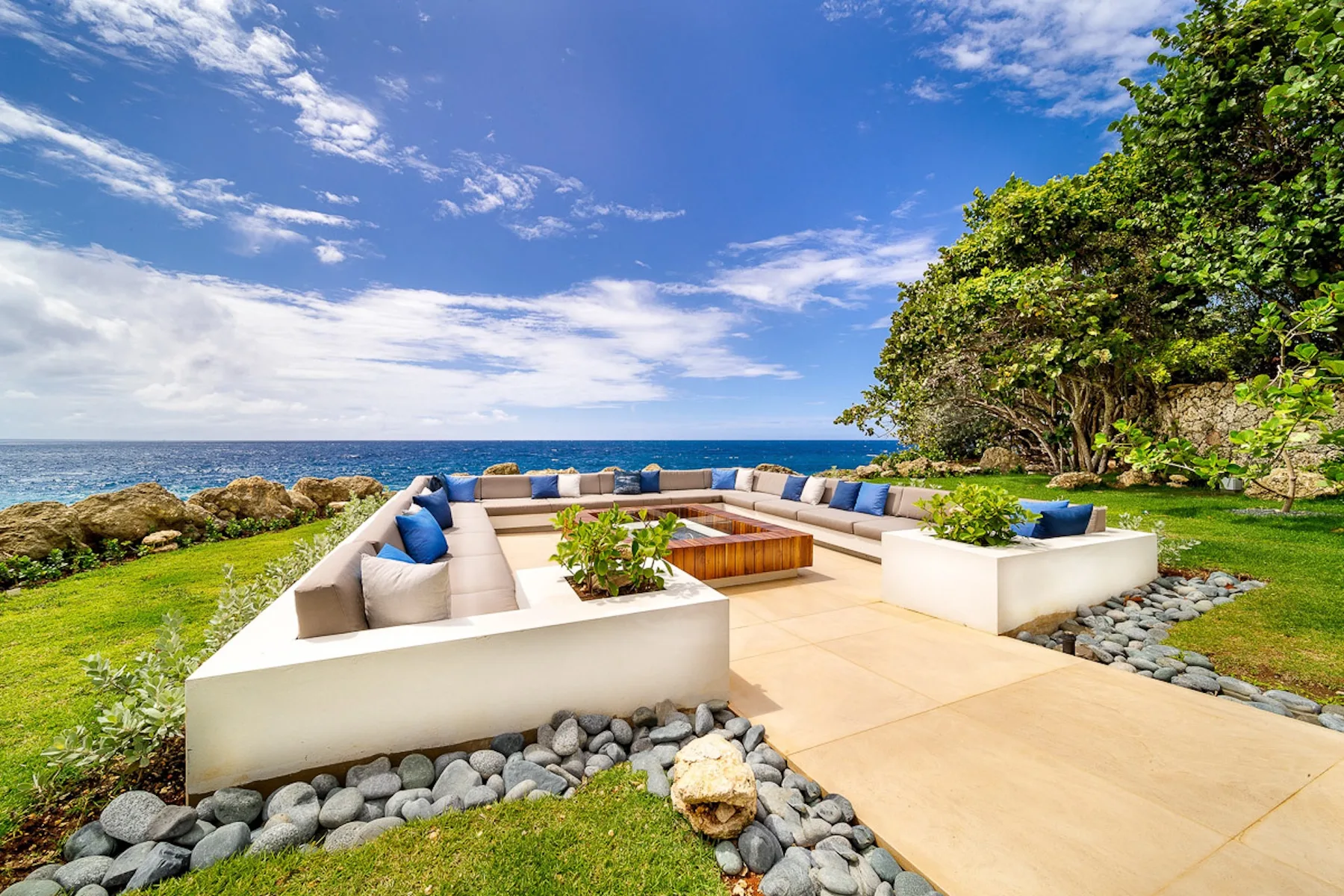 An outdoor lounge area beside the ocean, with cushioned seating around a low table.