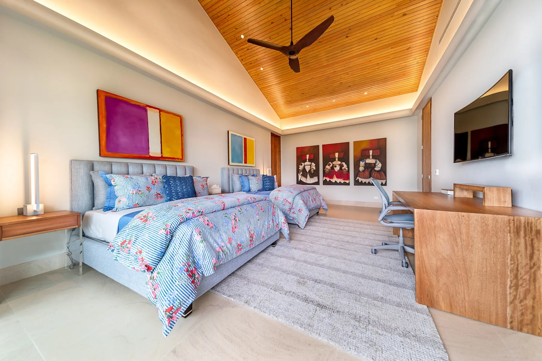 A bedroom with patterned bedding, a wooden ceiling, and a desk.