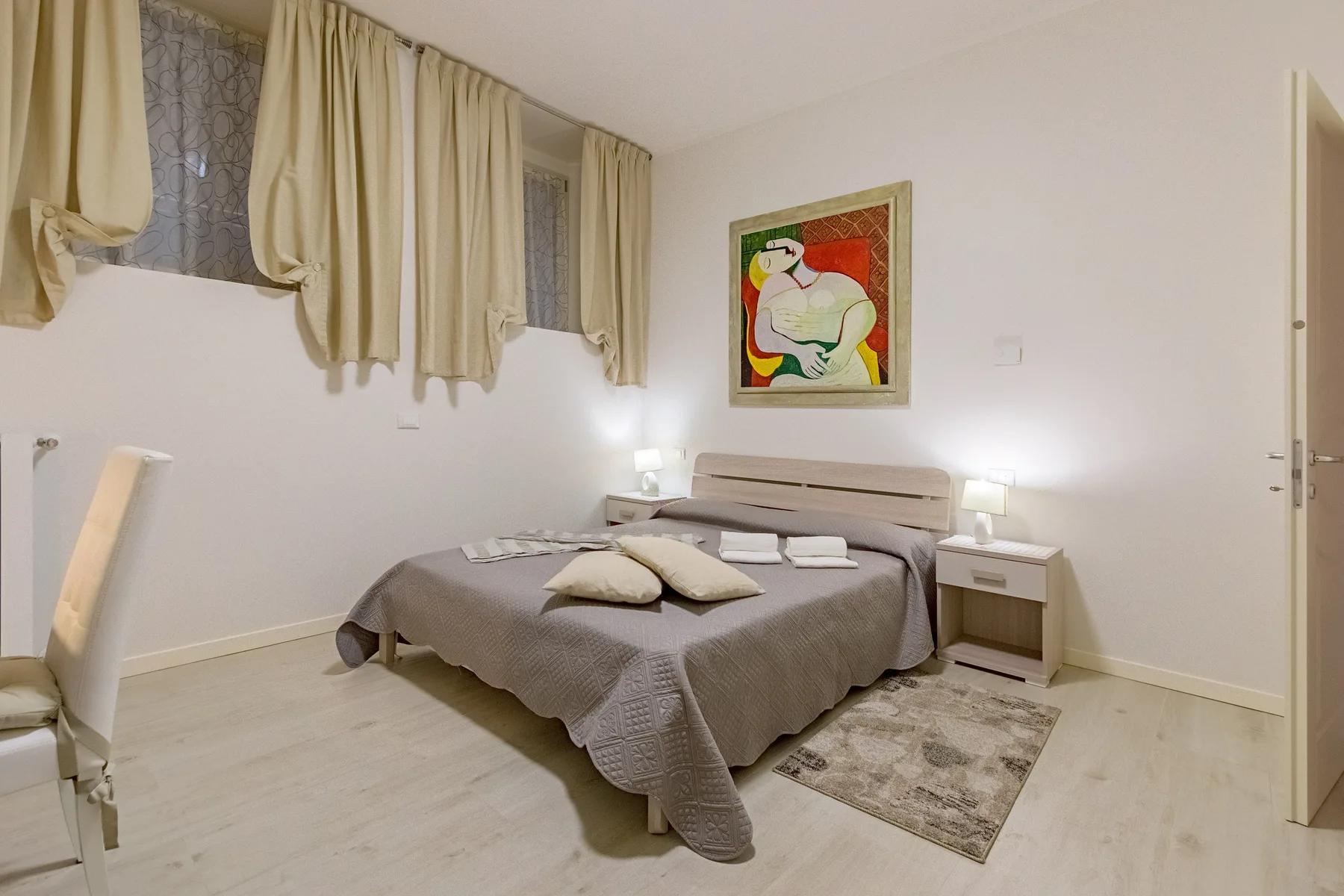Un dormitorio con una cama doble, mesitas de noche y una obra enmarcada.