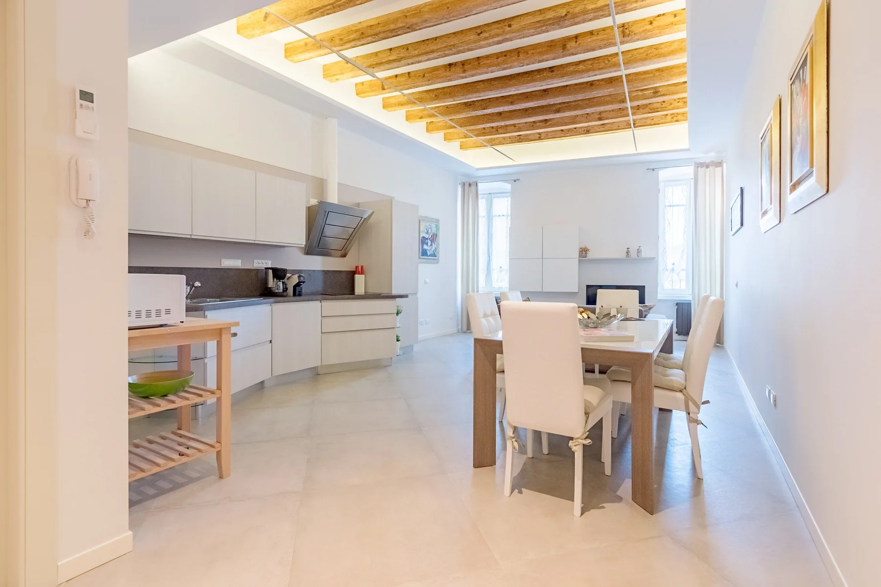 Una cocina luminosa con comedor y una mesa larga bajo vigas de techo expuestas.