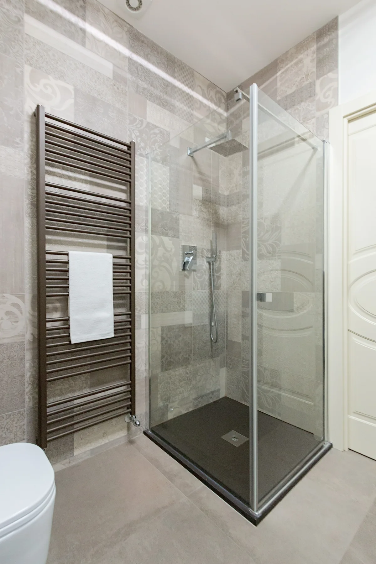 Un baño alicatado con una ducha de cristal y un toallero calefactable.