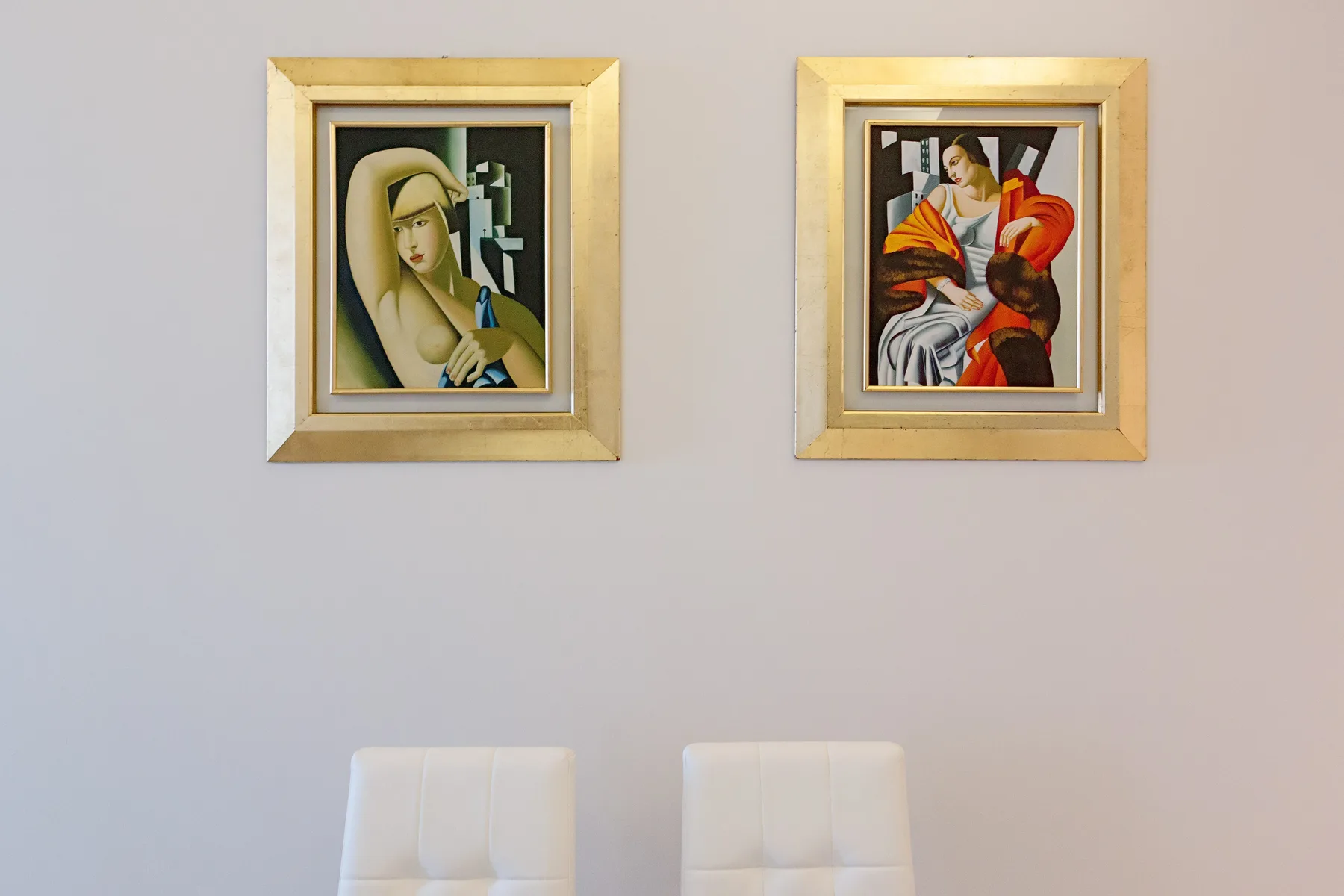 Una pared clara muestra dos obras enmarcadas sobre la parte superior de unos asientos blancos.