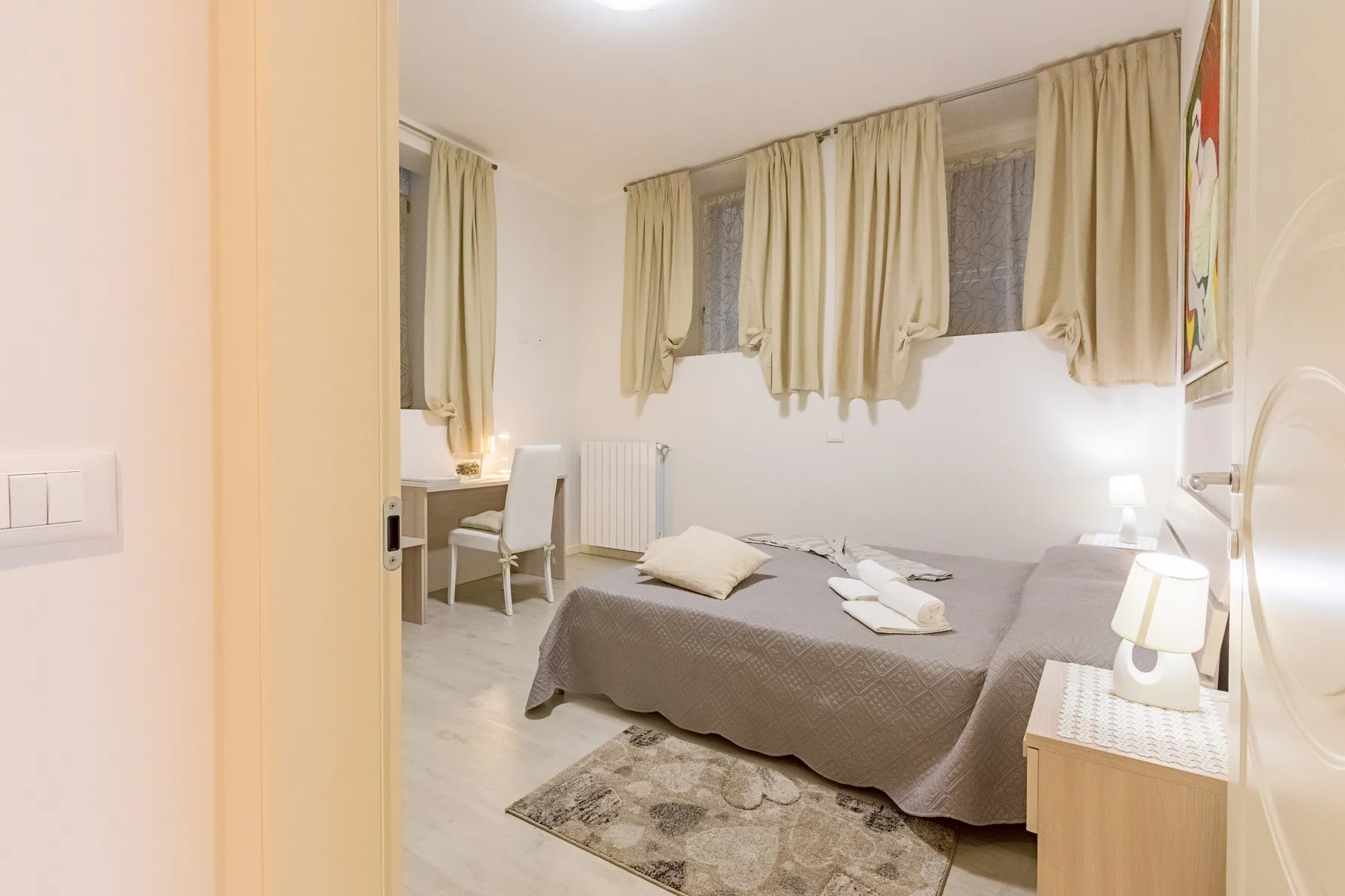Un dormitorio con una cama doble, una mesita de noche y ventanas con cortinas.