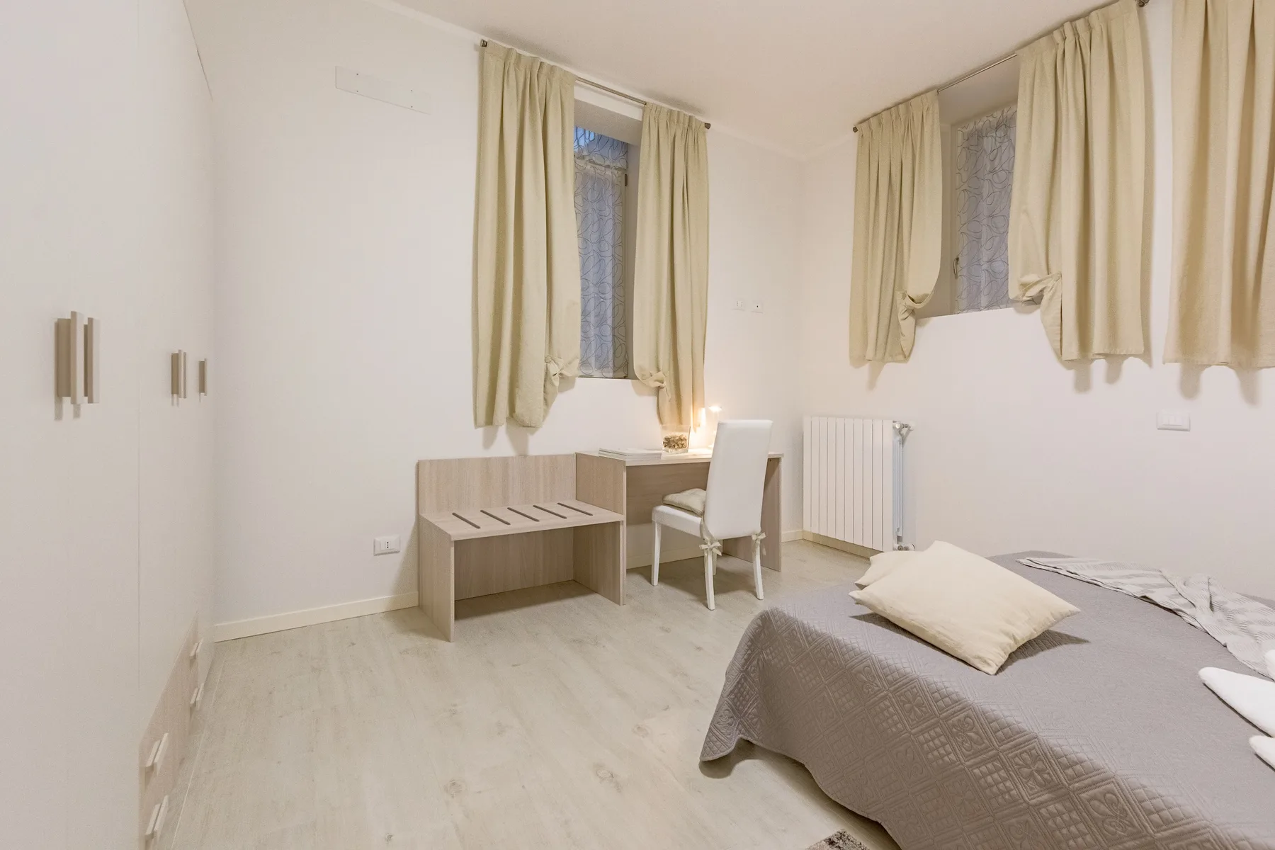 Un dormitorio con cama, escritorio y silla junto a ventanas con cortinas.