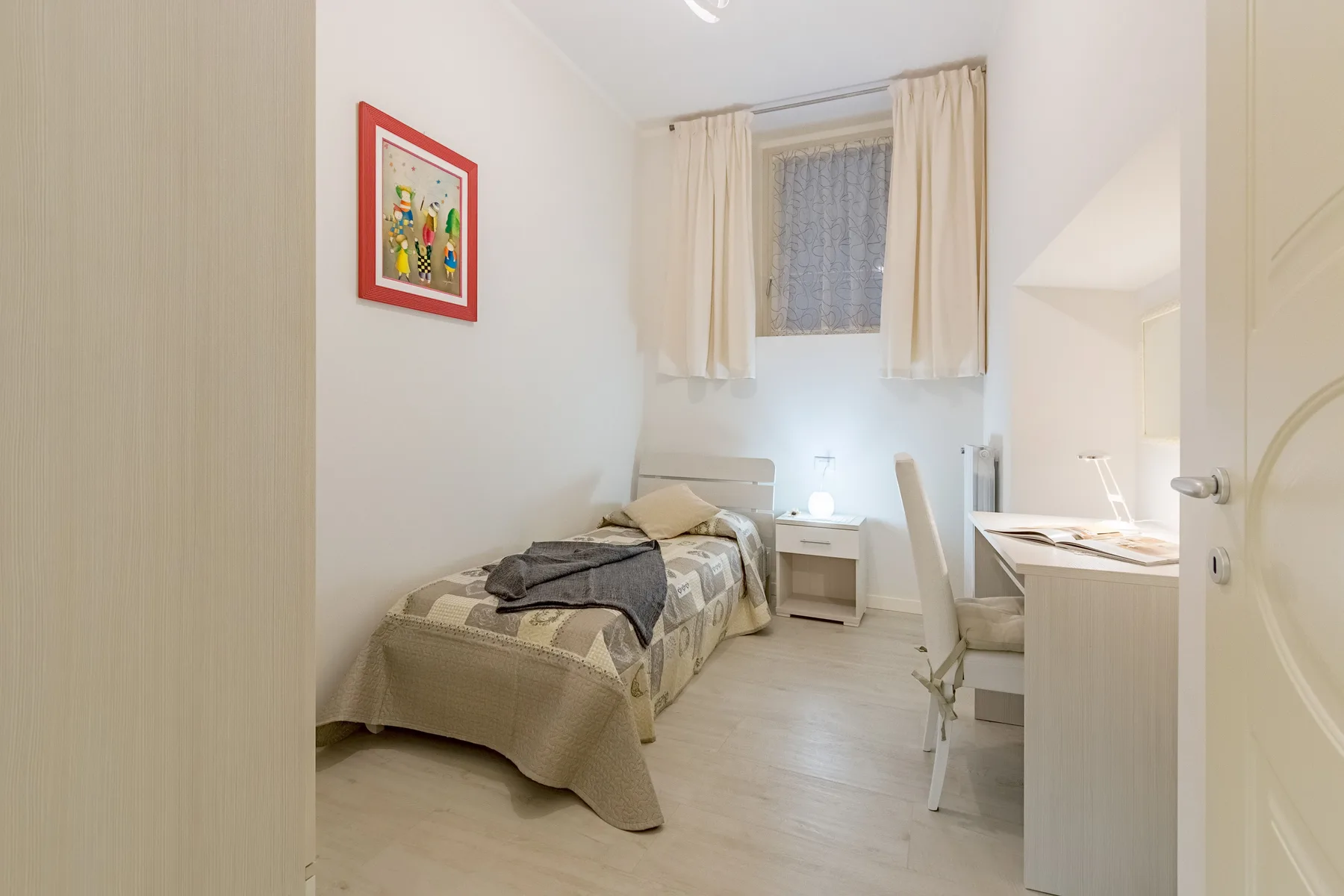 Un dormitorio con una cama individual, un escritorio y una ventana con cortinas.