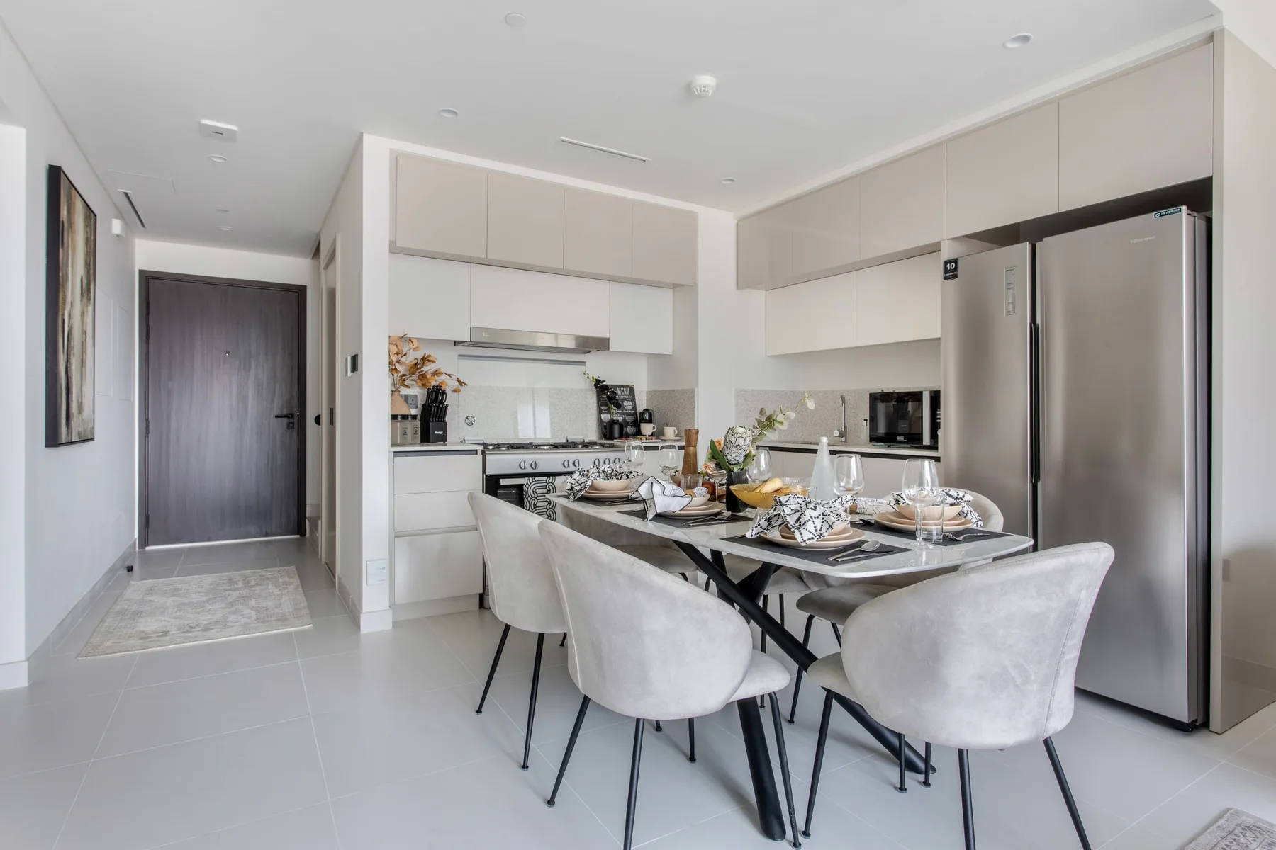 Una cocina y comedor luminosos con mesa, asientos y electrodomésticos de acero inoxidable.