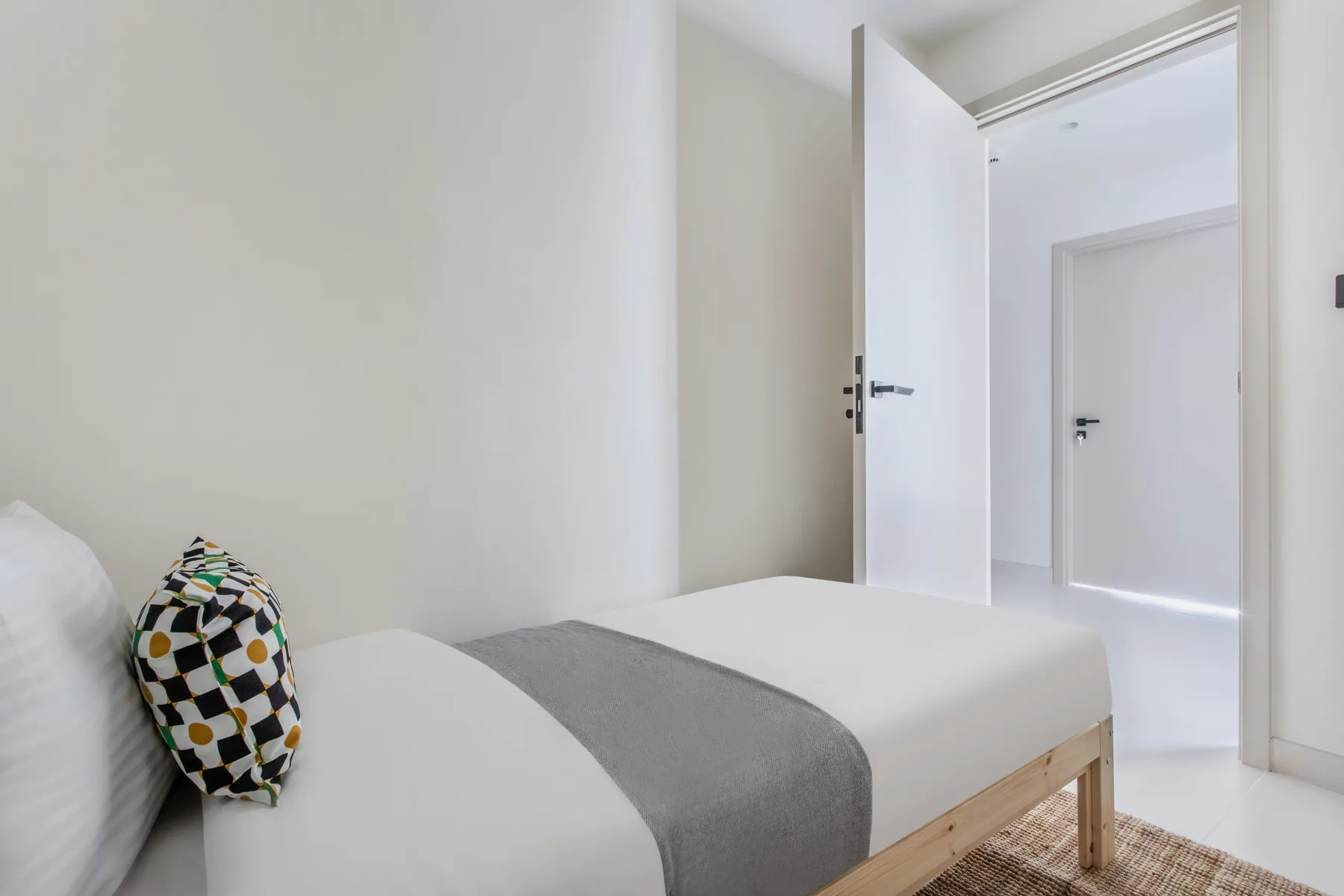 Un dormitorio con la cama tendida y una puerta abierta al pasillo.