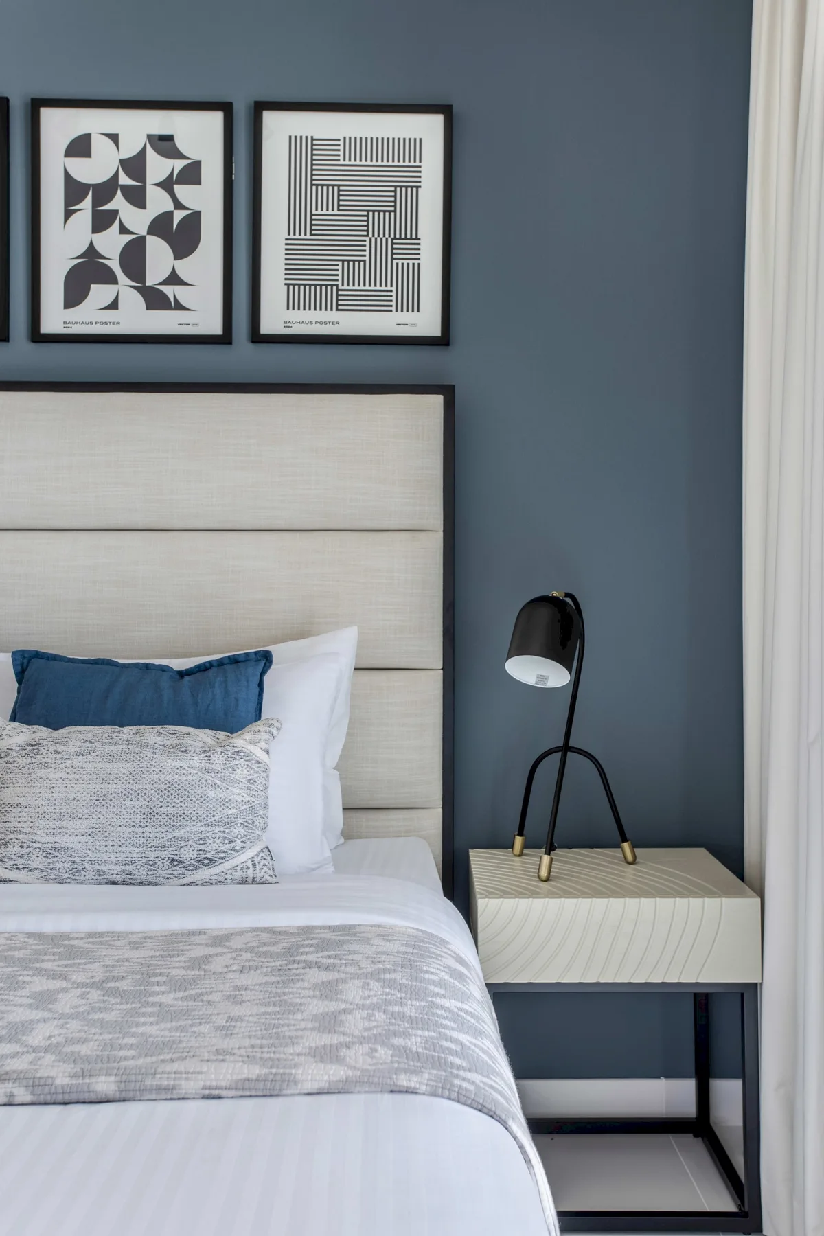 Un dormitorio con una cama tendida, láminas enmarcadas y una lámpara de noche.
