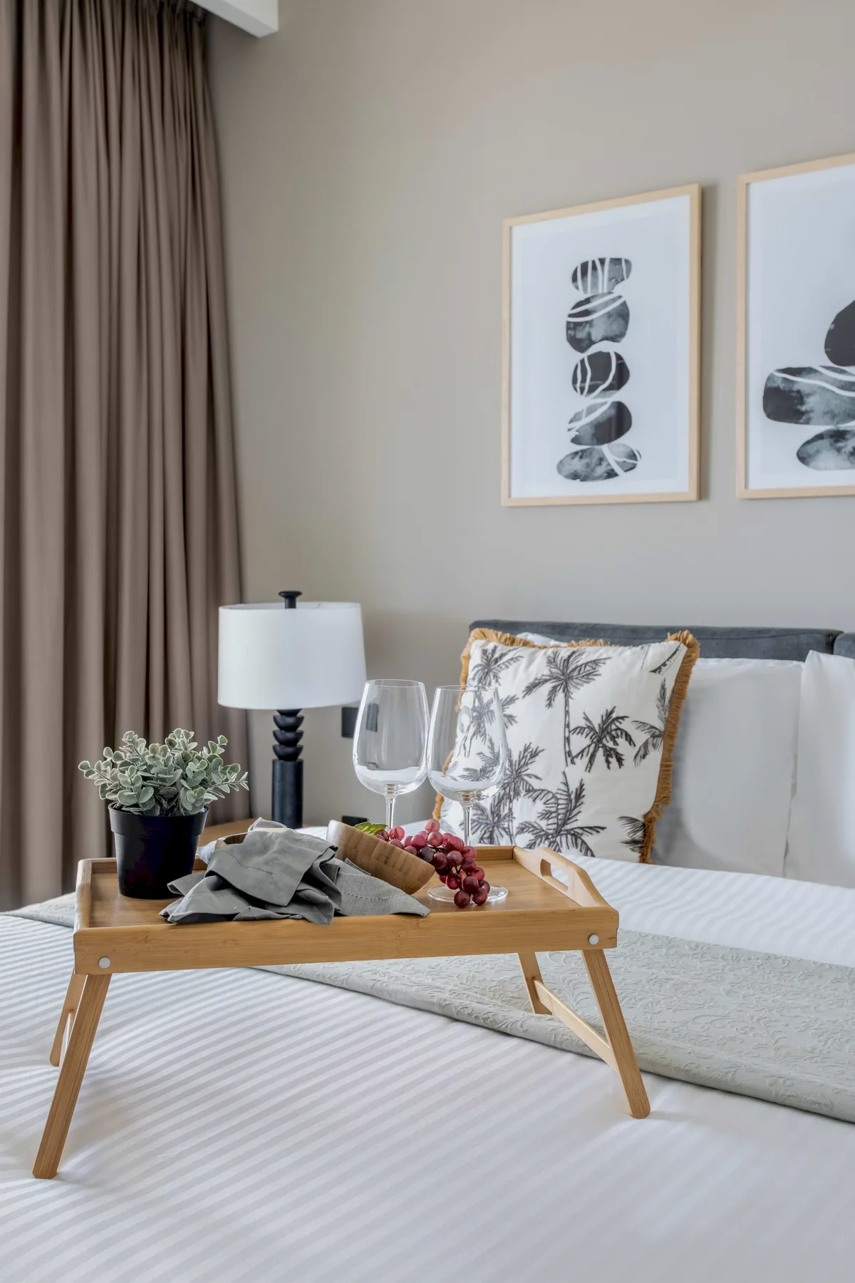 Un dormitorio con una cama, láminas abstractas enmarcadas y una bandeja de madera sobre la ropa de cama.