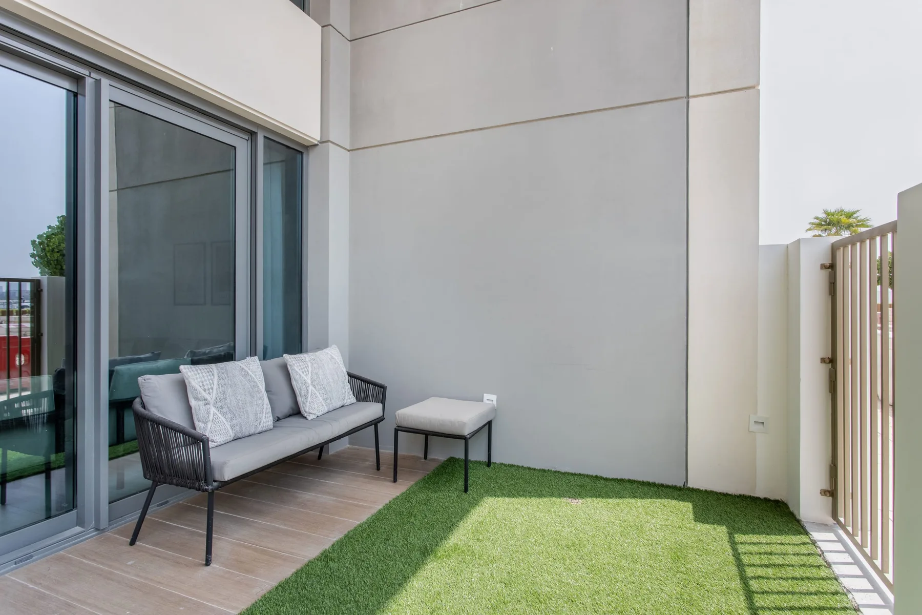 Una pequeña zona de estar al aire libre junto a puertas corredizas de vidrio y un área de césped artificial.