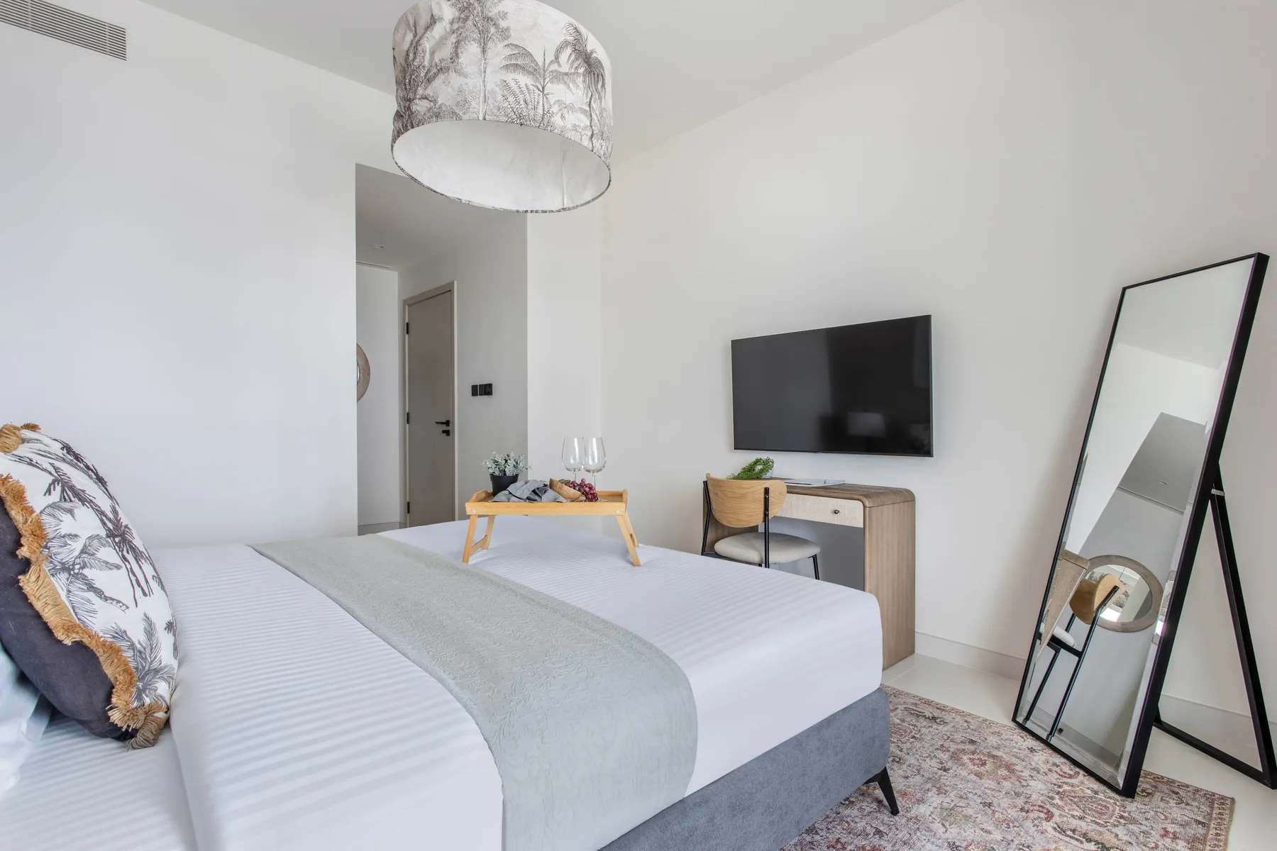 Un dormitorio luminoso con una cama bien hecha y un televisor en la pared.