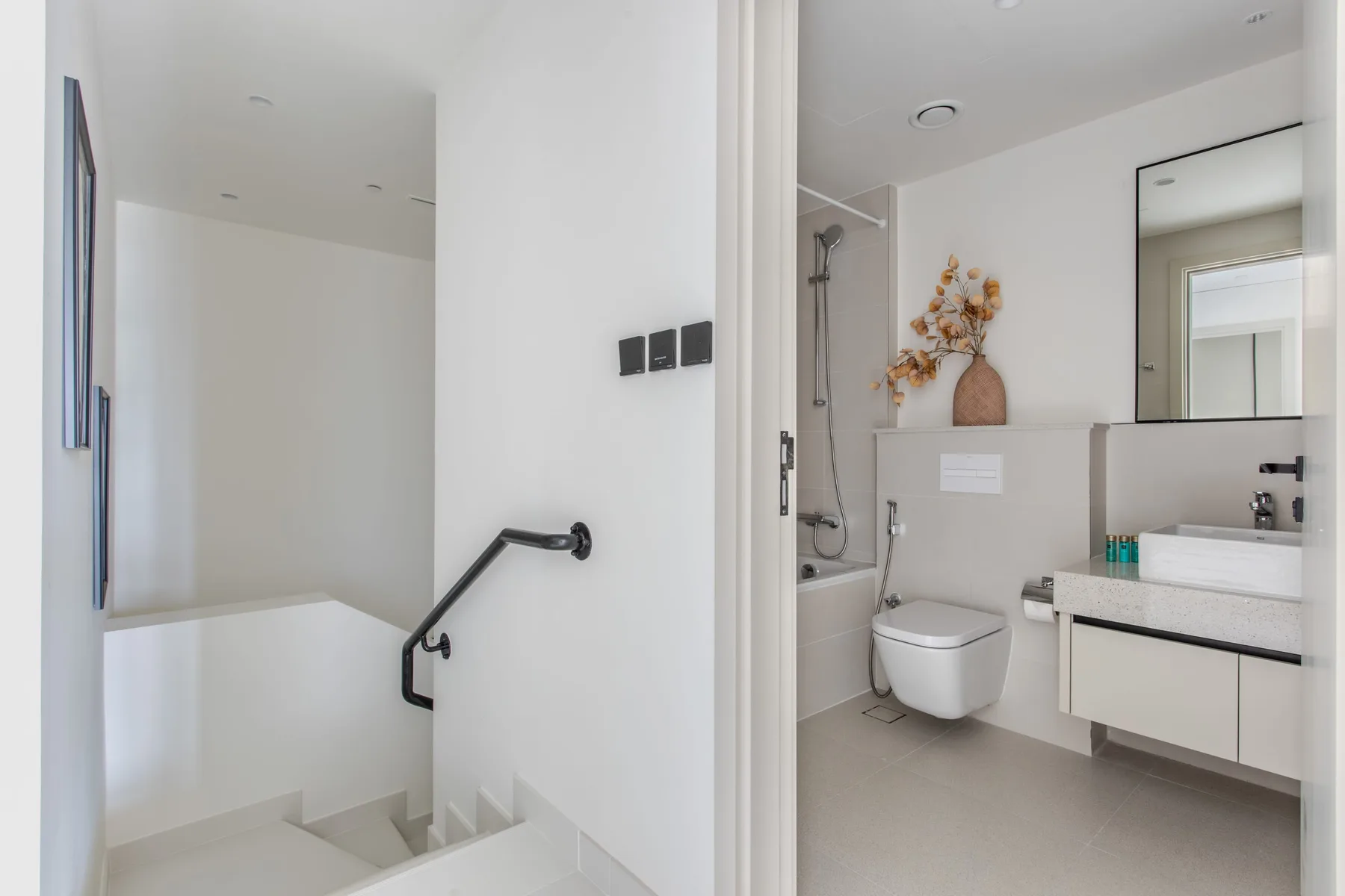 Un baño luminoso con lavabo, espejo y ducha junto a una escalera.