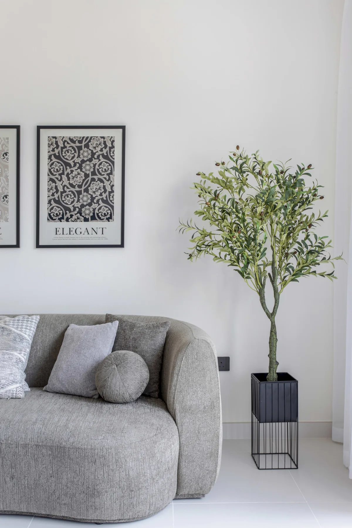 Sala de estar con un sofá gris, cuadros en la pared y un árbol en maceta.