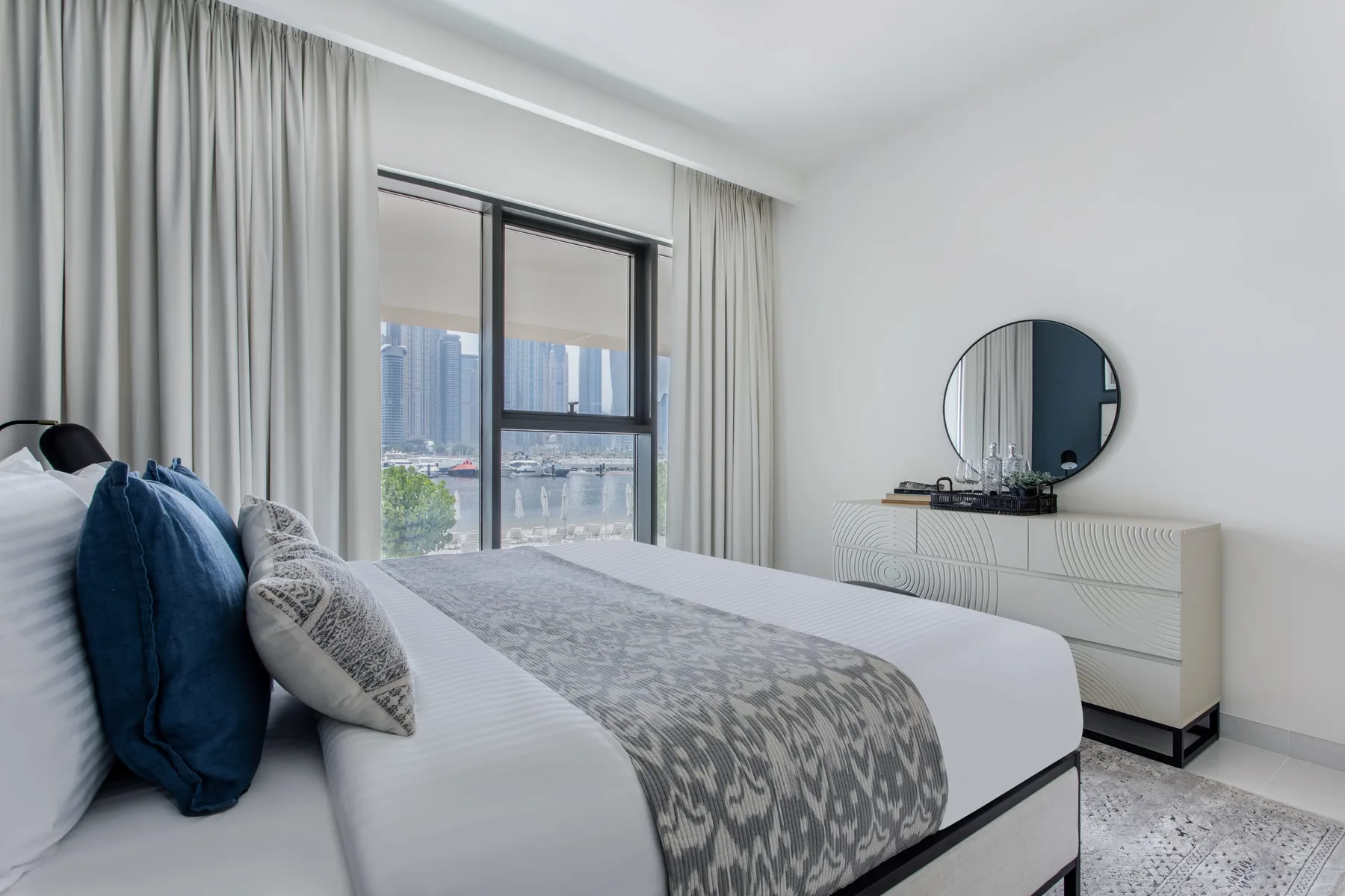 Un dormitorio con una cama tendida, cortinas y una ventana con vistas a edificios de la ciudad.