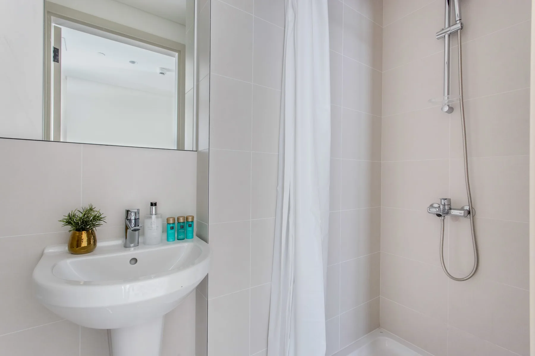Un baño luminoso con lavabo, espejo y ducha.