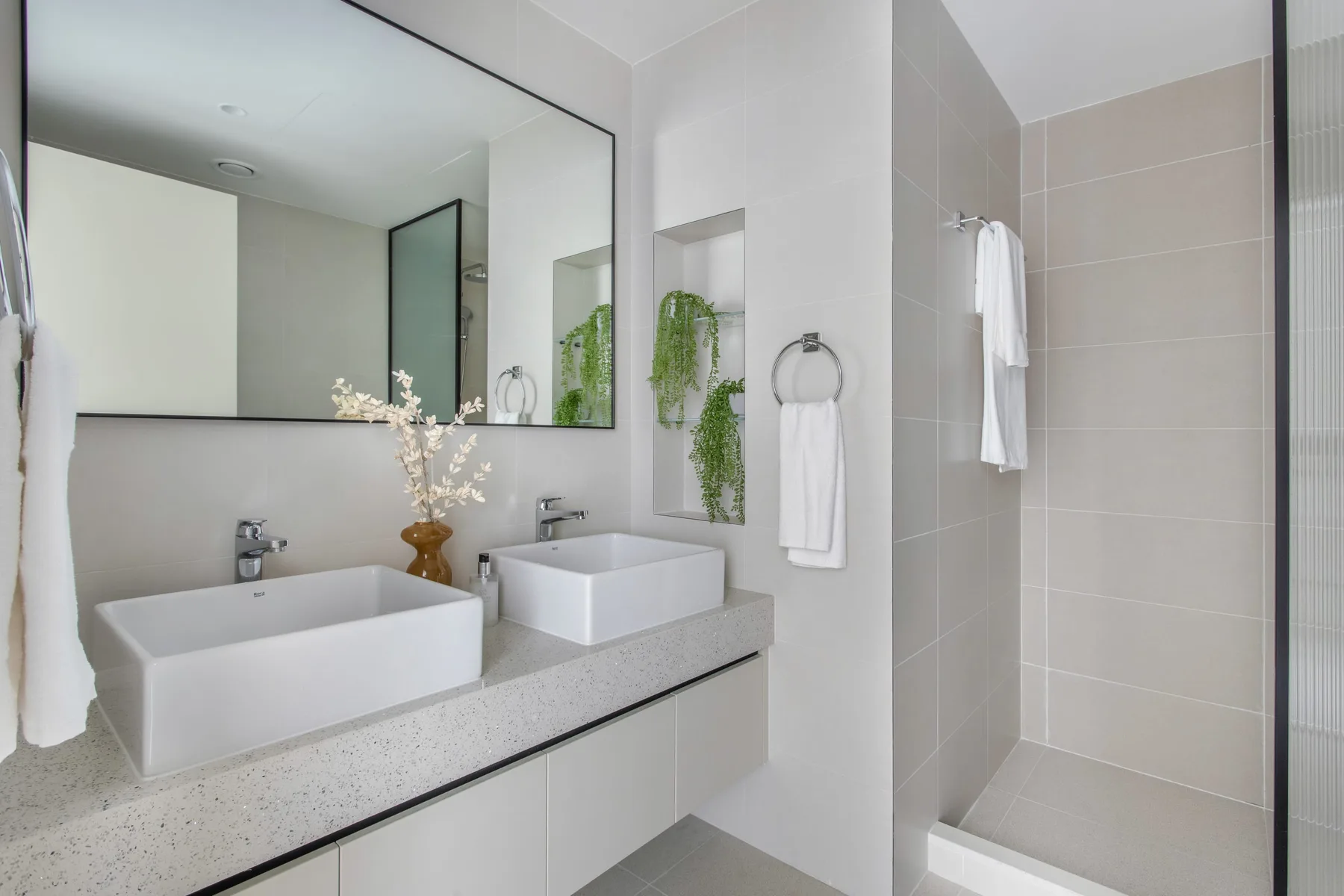 Un baño luminoso con lavabo doble, espejo de pared y ducha.