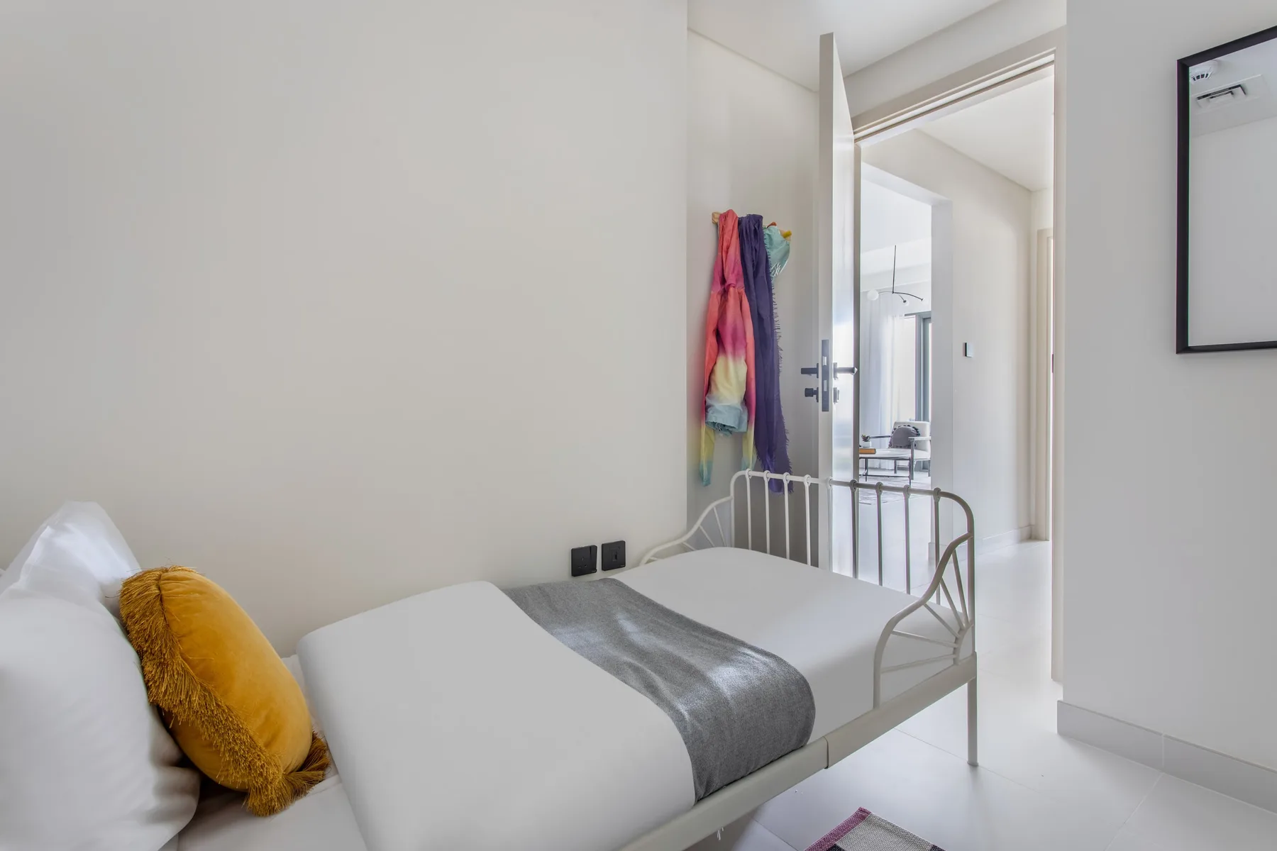 Un dormitorio con una cama individual y ropa de colores colgada junto a la puerta.