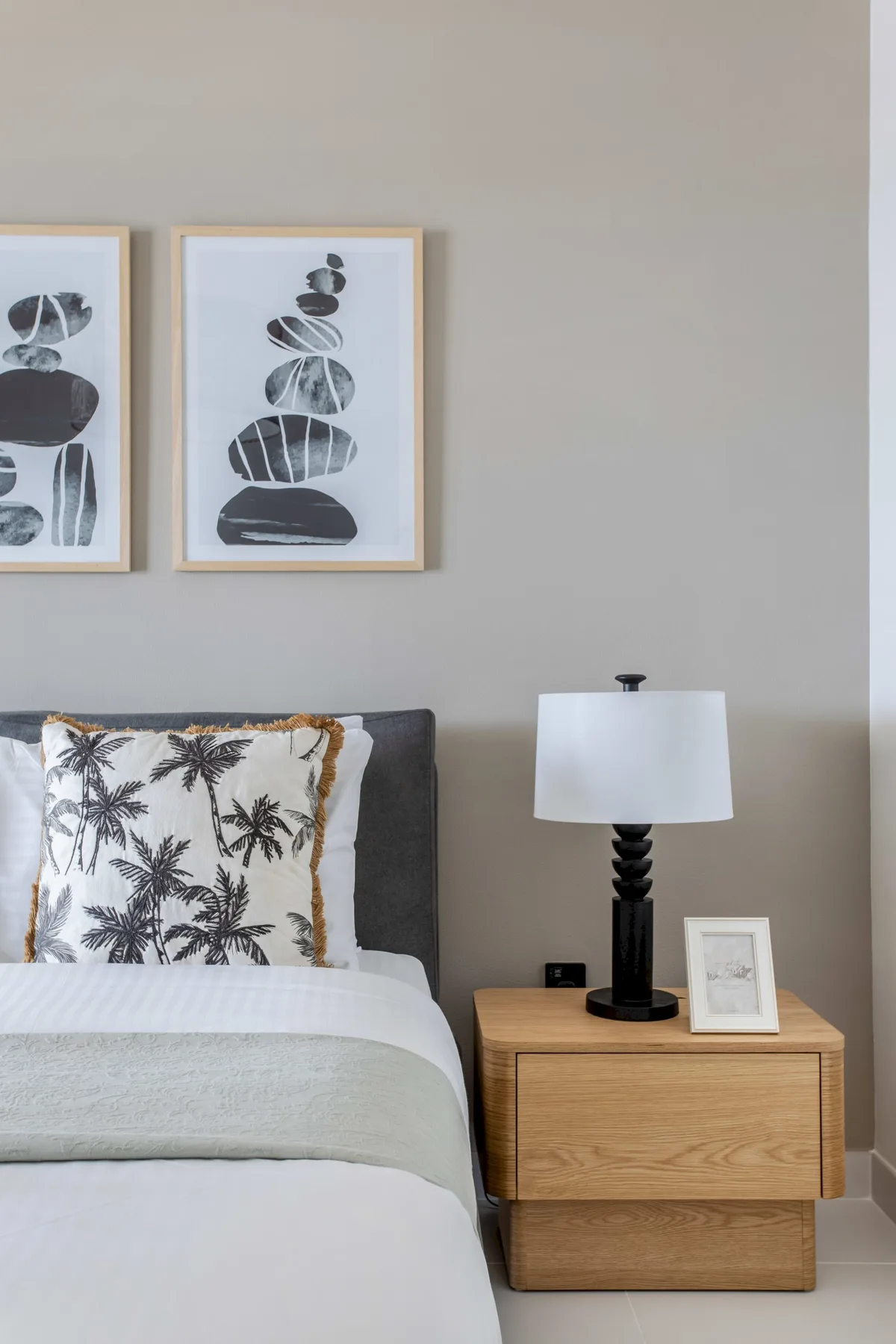 Un dormitorio con una cama tendida, cuadros enmarcados y una lámpara de mesita.