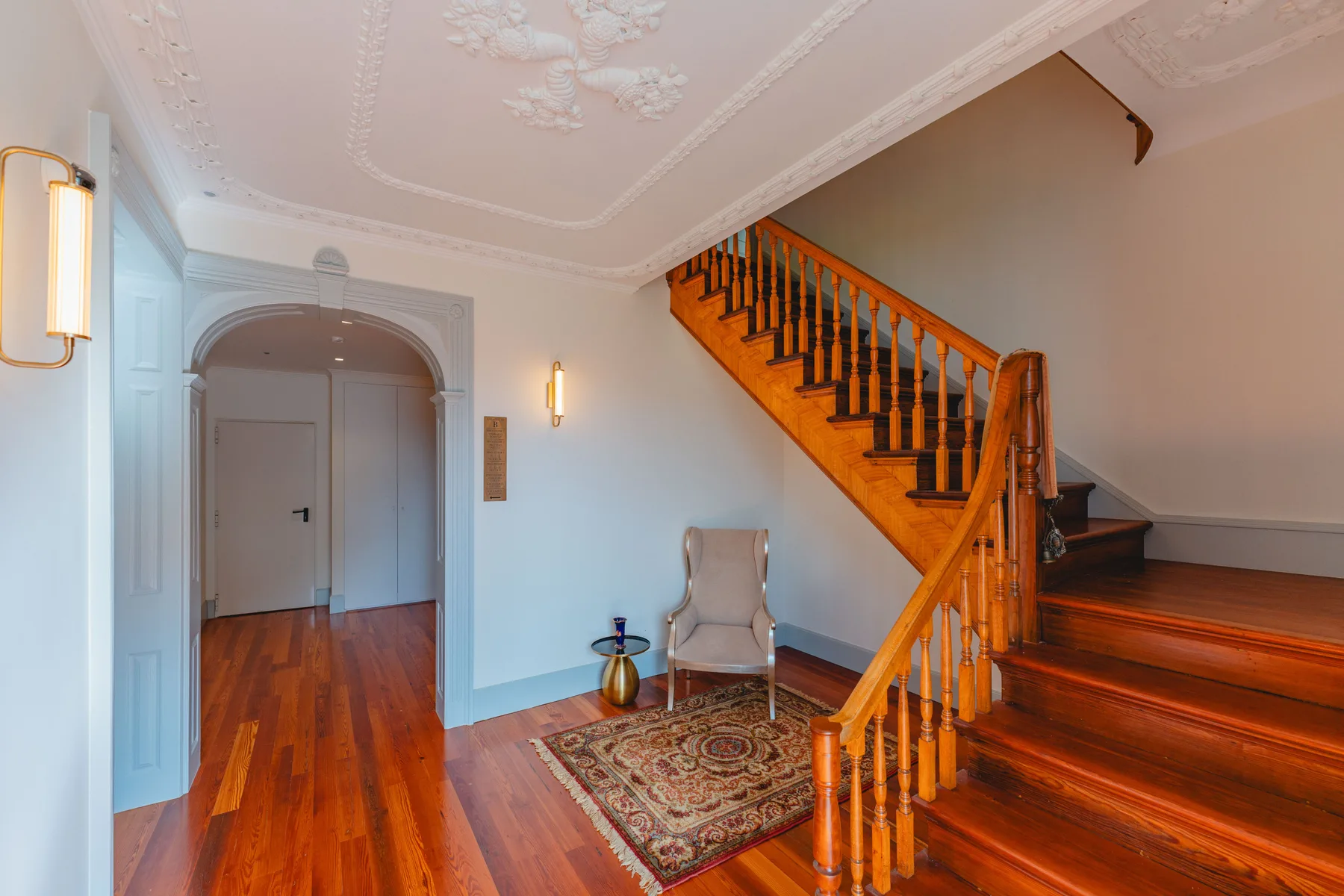 Un pasillo interior con una escalera de madera y una pequeña zona para sentarse.