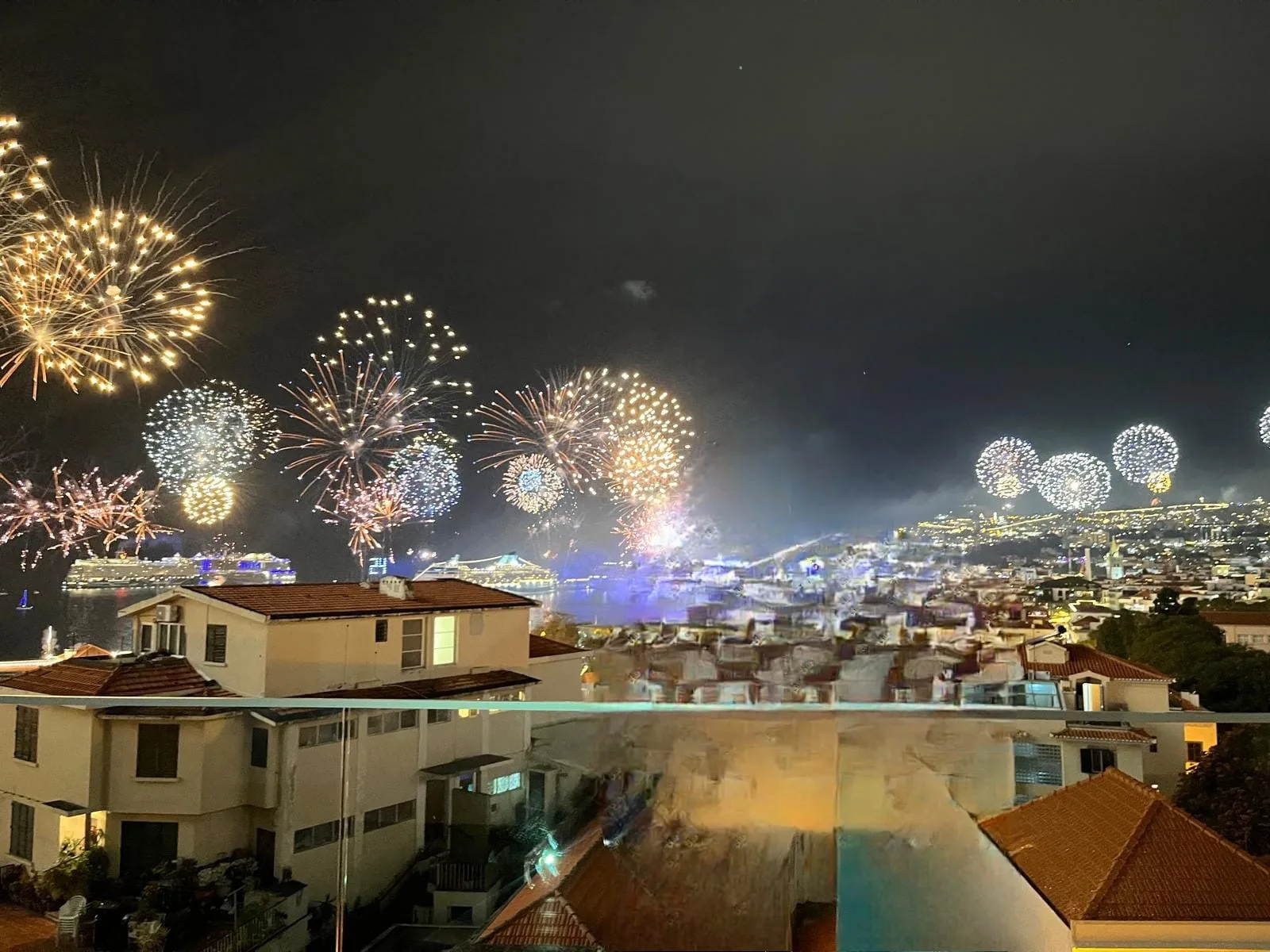 Un paisaje urbano nocturno muestra fuegos artificiales sobre los tejados.