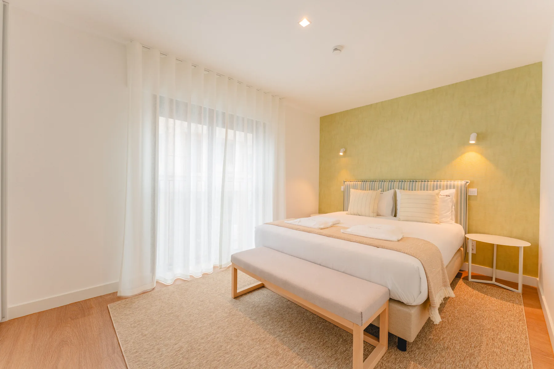 Un dormitorio luminoso con una cama bien hecha y un banco a sus pies.