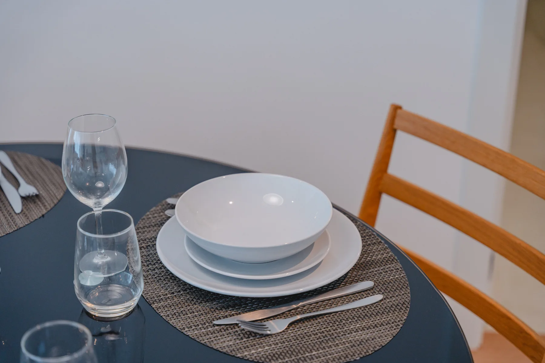 Una mesa de comedor está puesta con platos apilados, vasos y cubiertos.