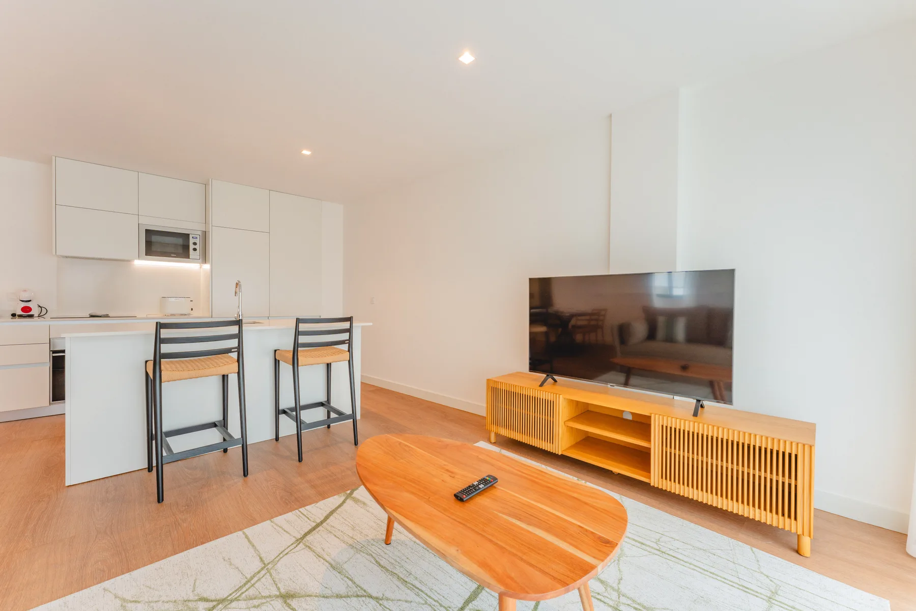 Una sala luminosa con televisor, mesa de centro y cocina abierta.