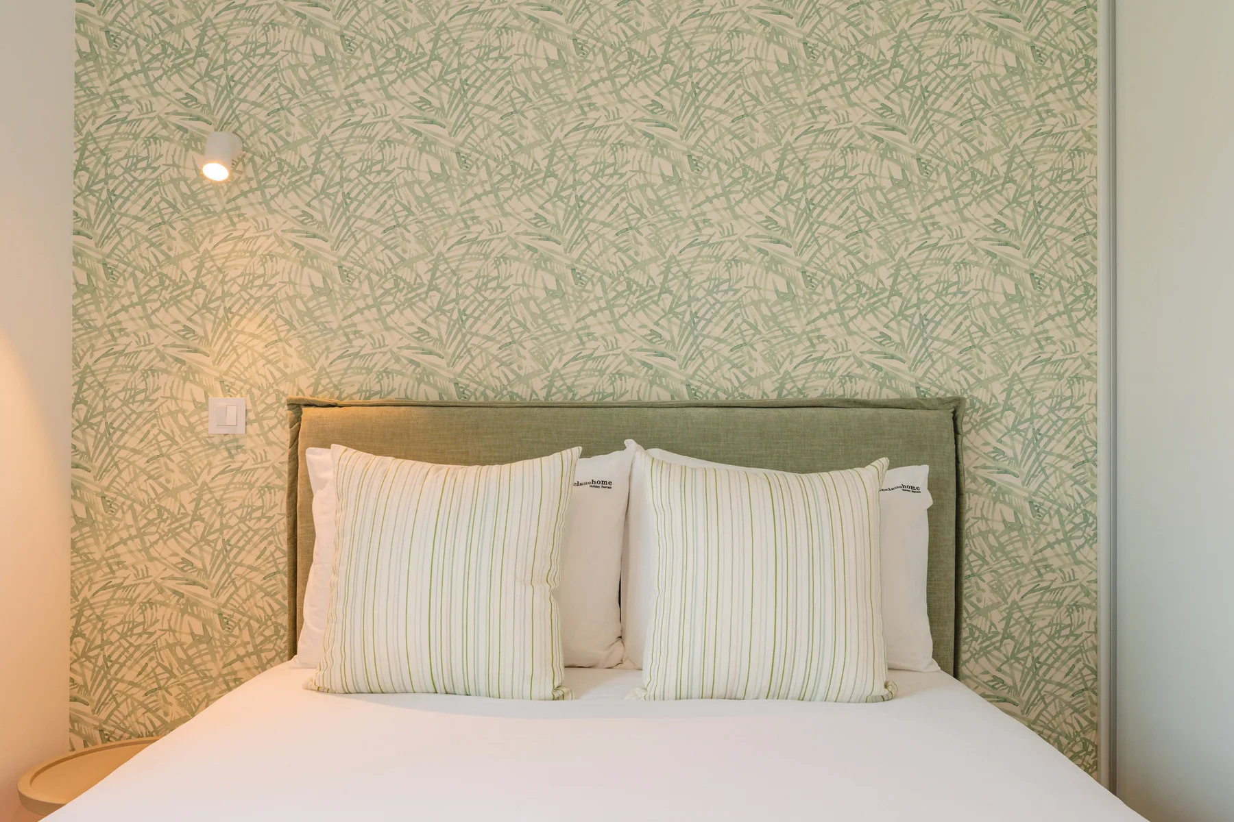 Un dormitorio con una cama frente a una pared verde estampada.
