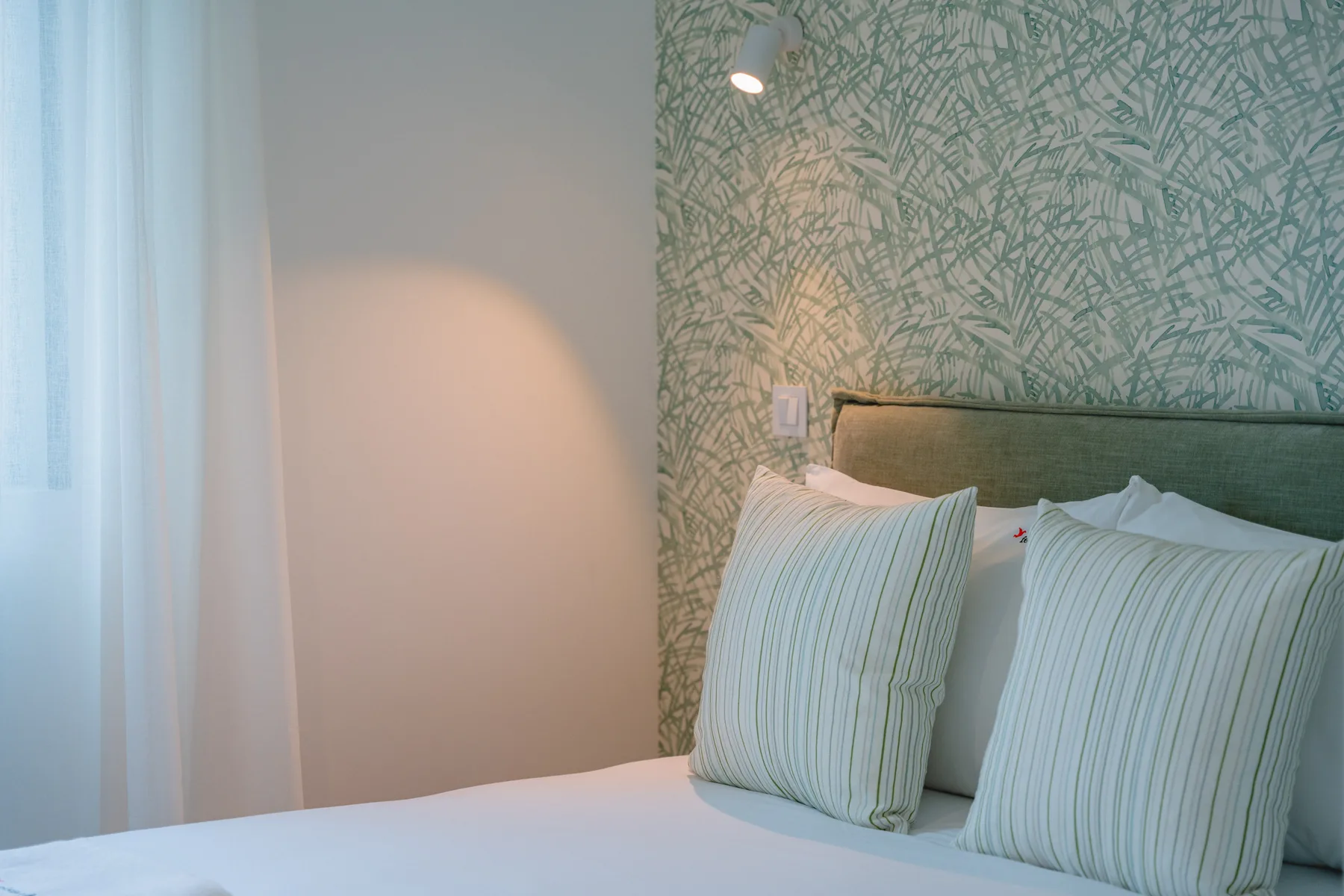 Dormitorio con una cama, cojines a rayas y papel pintado con motivos de hojas.