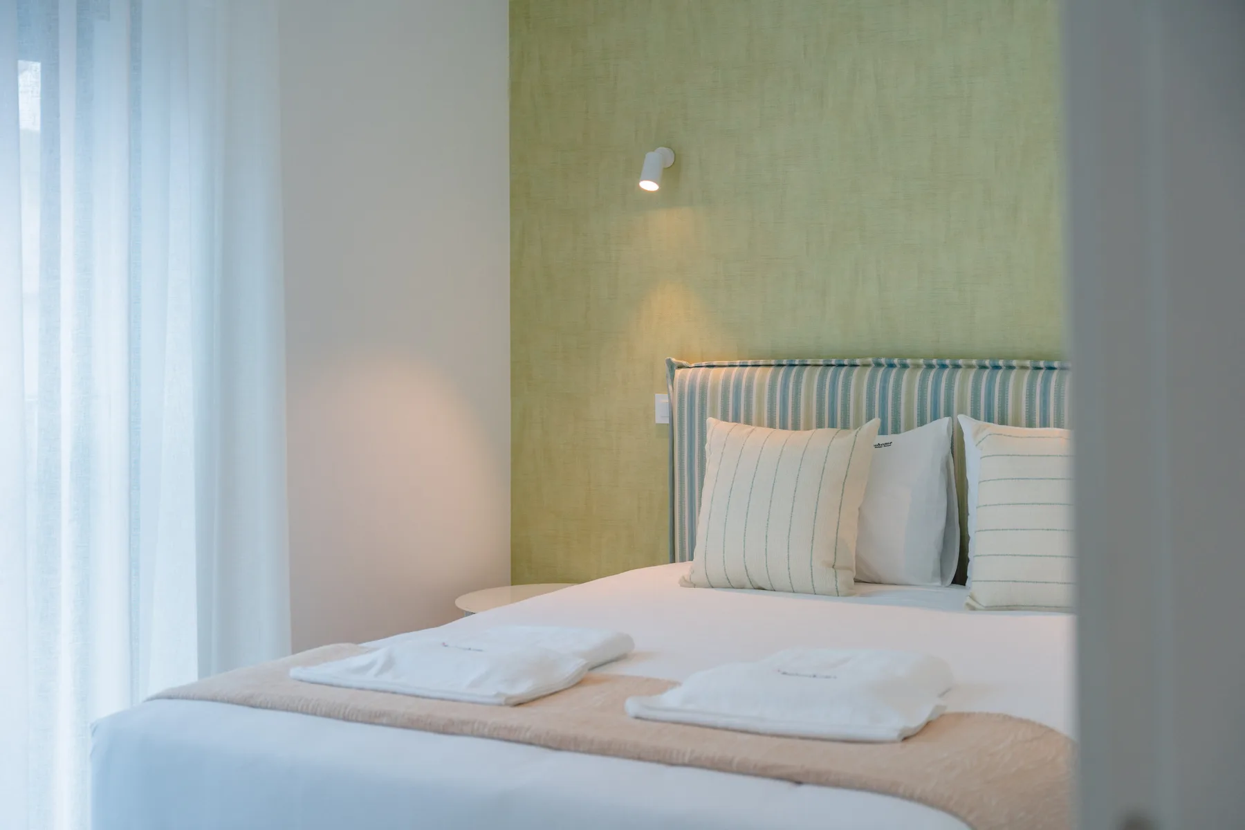 Un dormitorio con una cama bien arreglada junto a una ventana con cortinas.