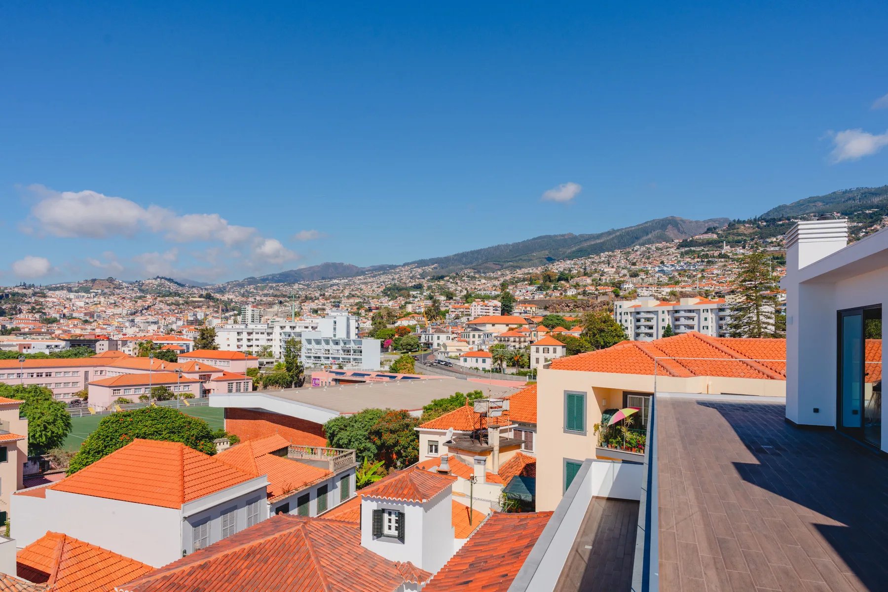 Vista de una ciudad en una ladera, con edificios de tejados rojos bajo un cielo azul despejado.