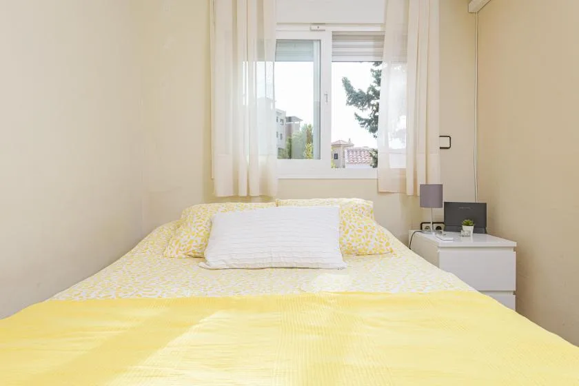 A bedroom with a bed beneath a window and a small bedside table.