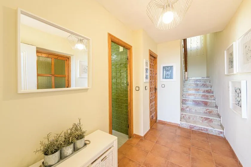 A bright interior hallway with terracotta-colored floor tiles and a staircase.