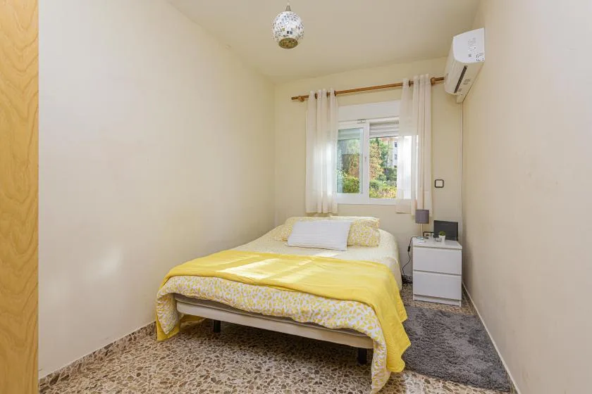 A bedroom with a bed dressed in yellow bedding beneath a window.