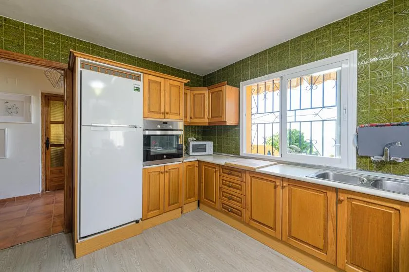 A kitchen with wooden cabinets, a refrigerator, and a sink beneath a large window.