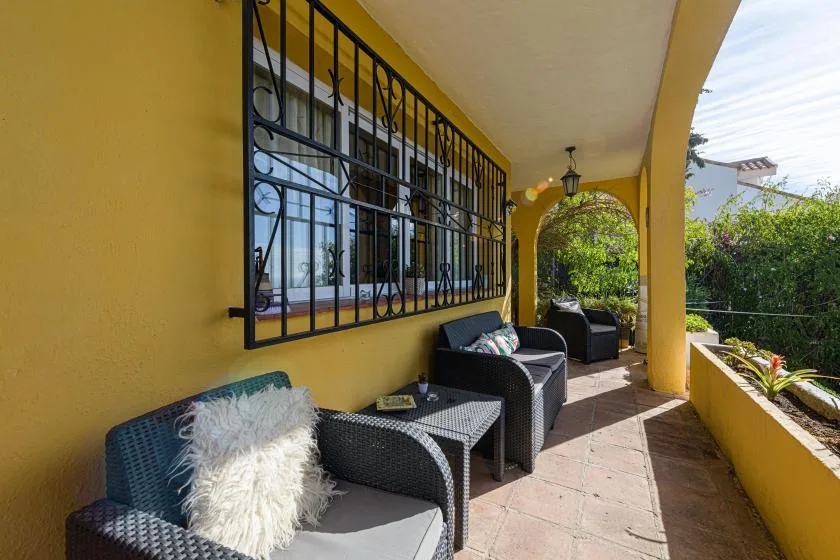 A covered patio with dark seating and barred windows along a yellow wall.