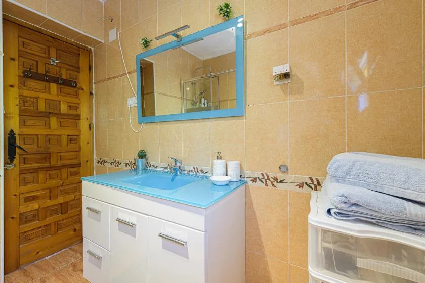 A tiled bathroom with a sink vanity, mirror, and wooden door.