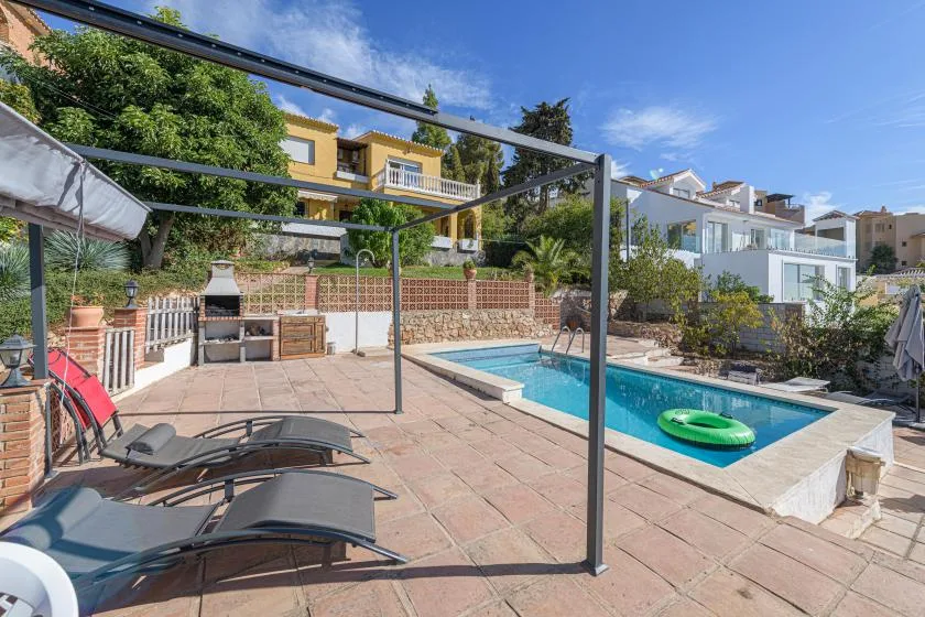 A sunny outdoor pool area with lounge seating and a paved patio.