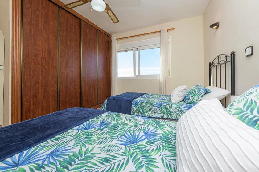 A bedroom with beds dressed in leafy patterned bedding and a window.