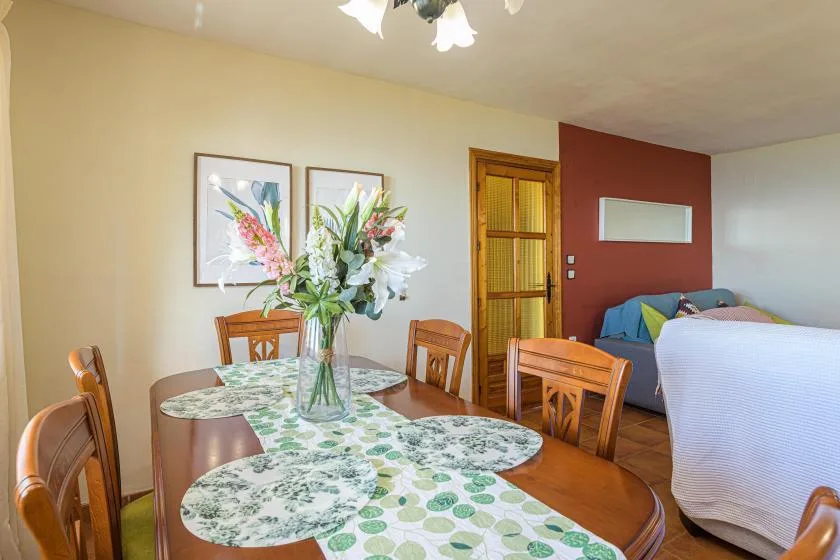 A bedroom with a bed, dining table, and flower arrangement.
