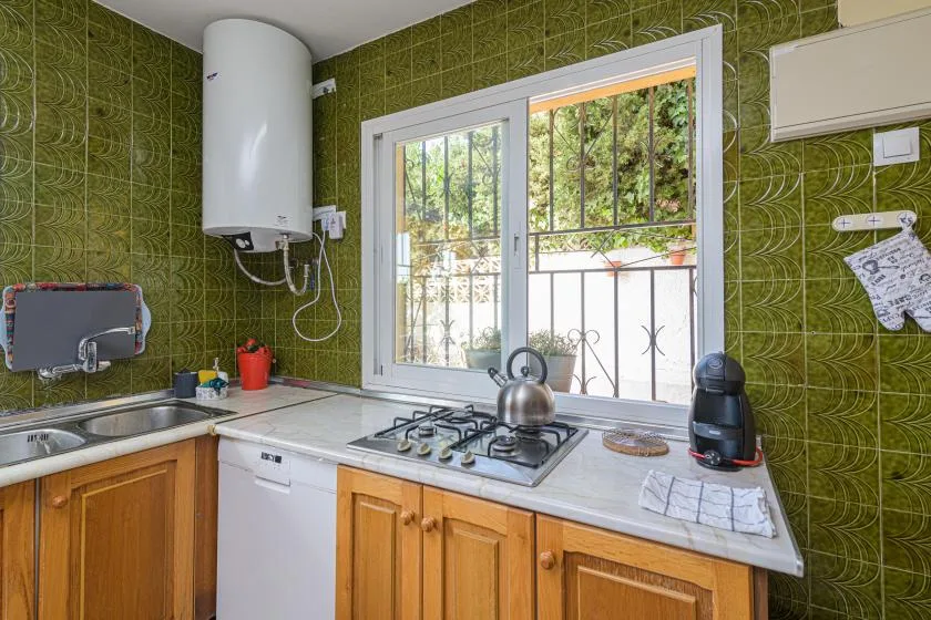 A tiled kitchen with wooden cabinets, a gas cooktop, and a window overlooking greenery.
