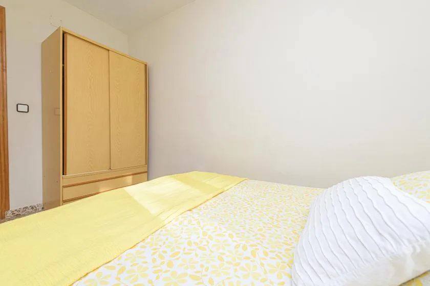 A bedroom with a bed covered in yellow patterned bedding and a wooden wardrobe.