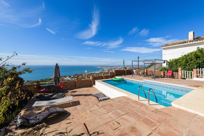 A swimming pool and tiled patio overlook the sea beneath a clear blue sky.