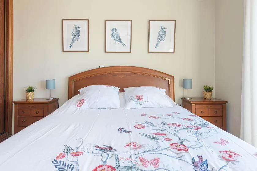 A bedroom with a wooden bed, floral bedding, and framed bird prints.