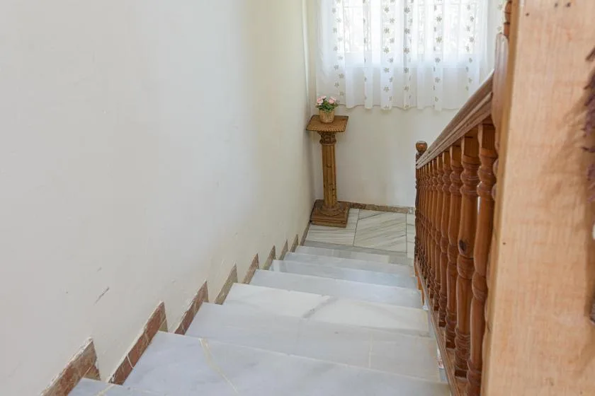 An indoor staircase descends beside a wooden railing toward a curtained window.