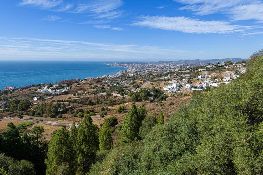 A coastal landscape with the sea, hillside vegetation, and buildings along the shore.