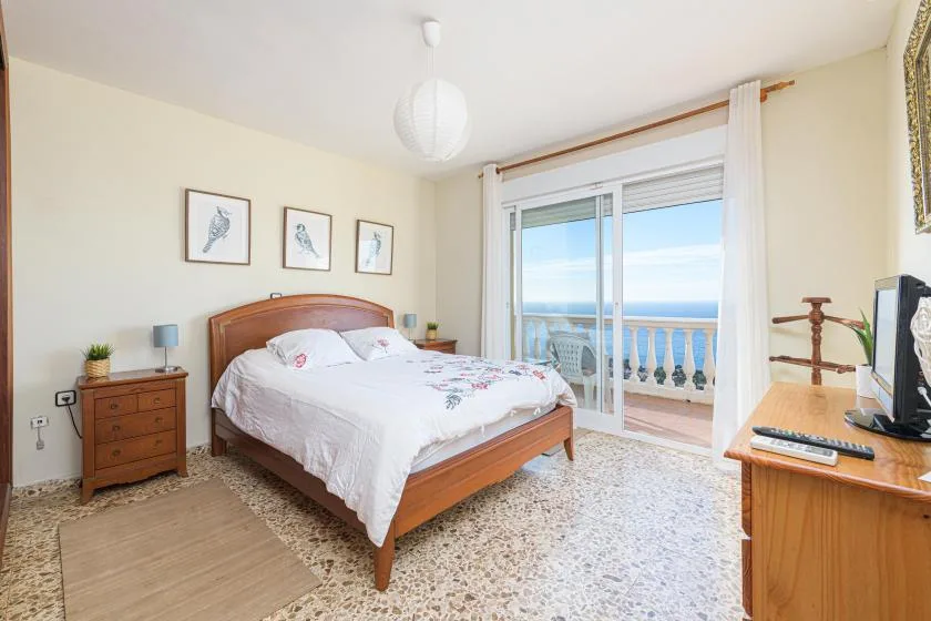 A bedroom with a wooden bed and sliding glass doors opening onto a balcony.