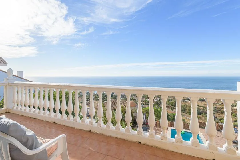 A balcony with white railing overlooks the sea beneath a blue sky.